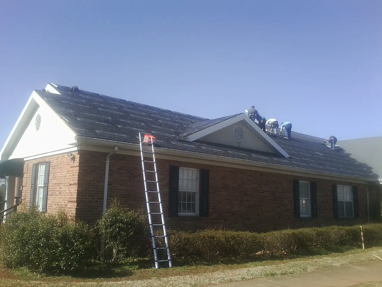 Crew tearing shingles off a brick ranch roof with a ladder set — Emergency Roof Repair work by our crew in Bethany