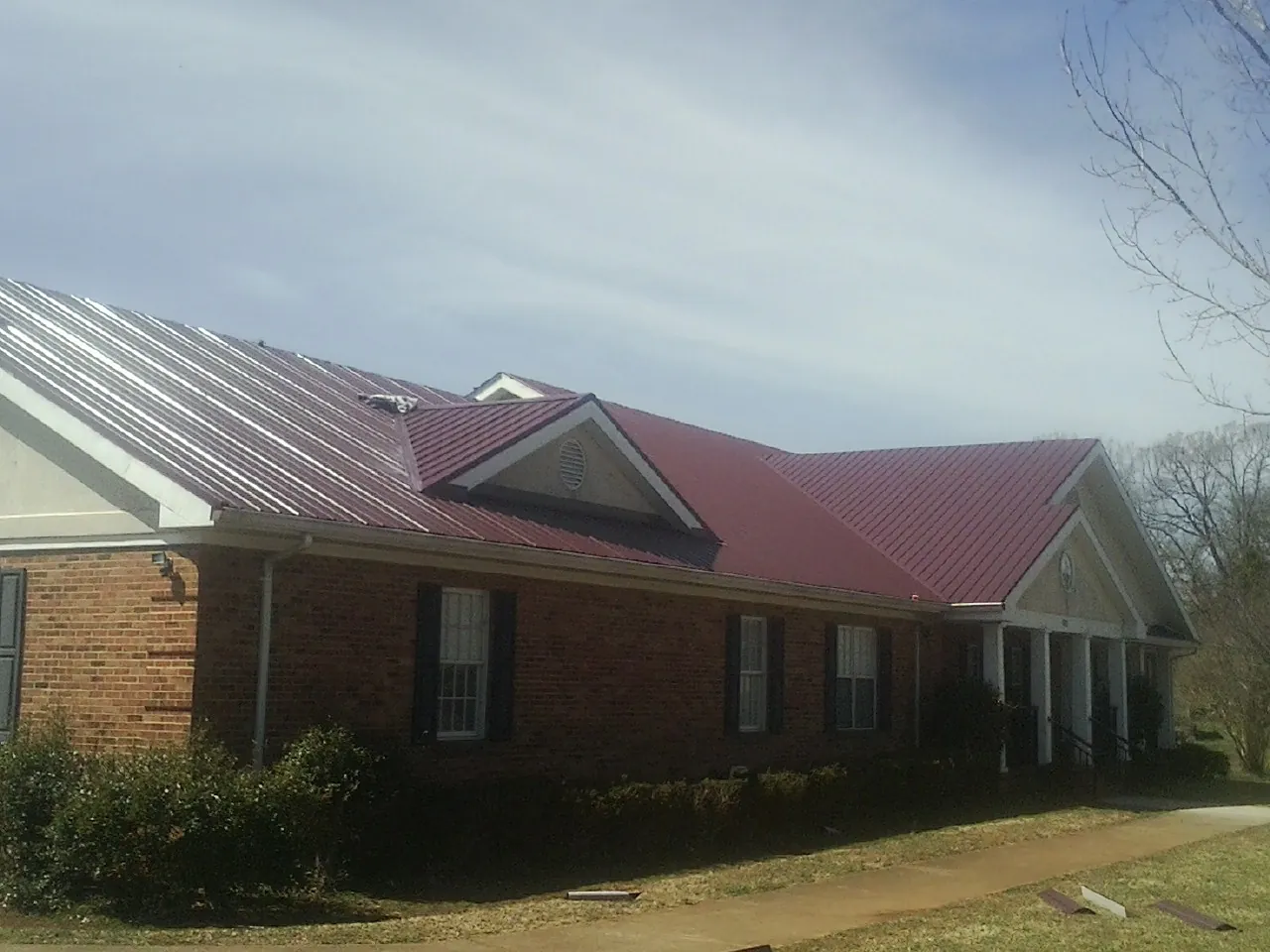 Red metal roof with gabled entries on a long brick building, from a Hail Damage Roof Repair job in Bethany