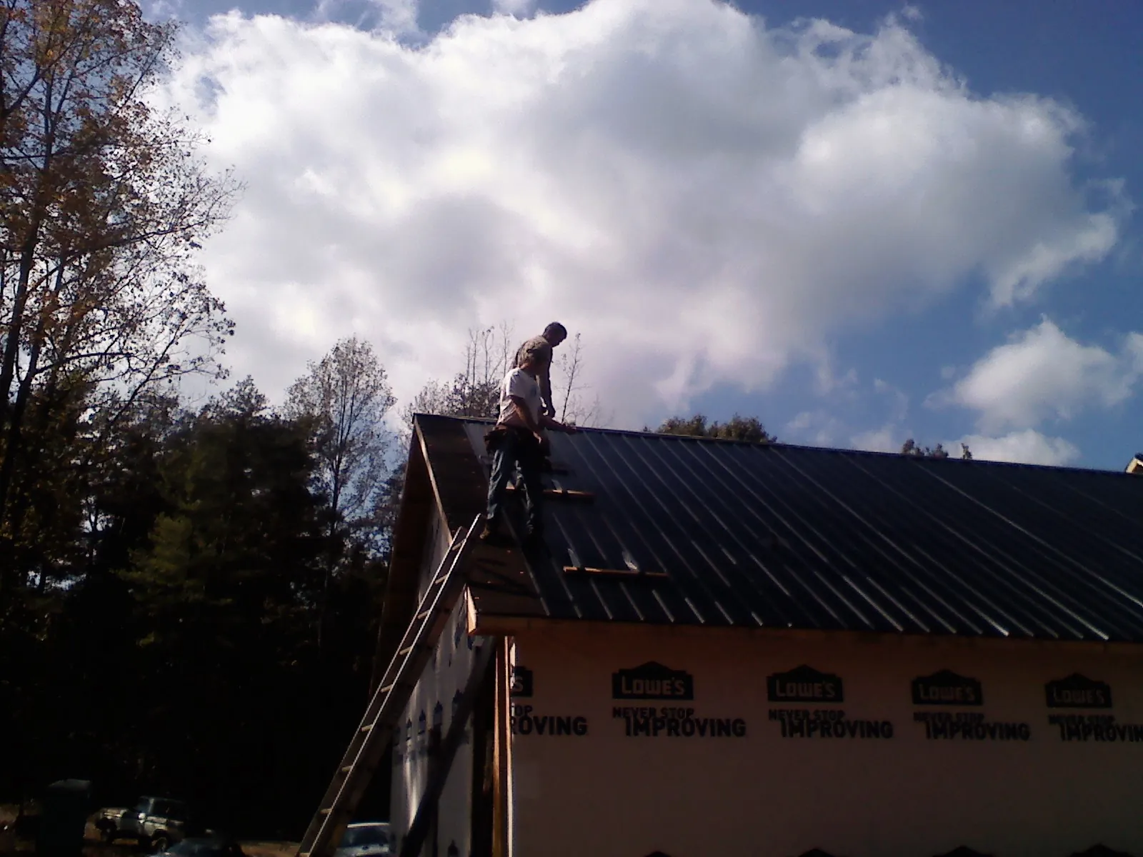 Roofer fastening dark metal panels high against a cloudy sky, from a Roof Inspection job in Bethany
