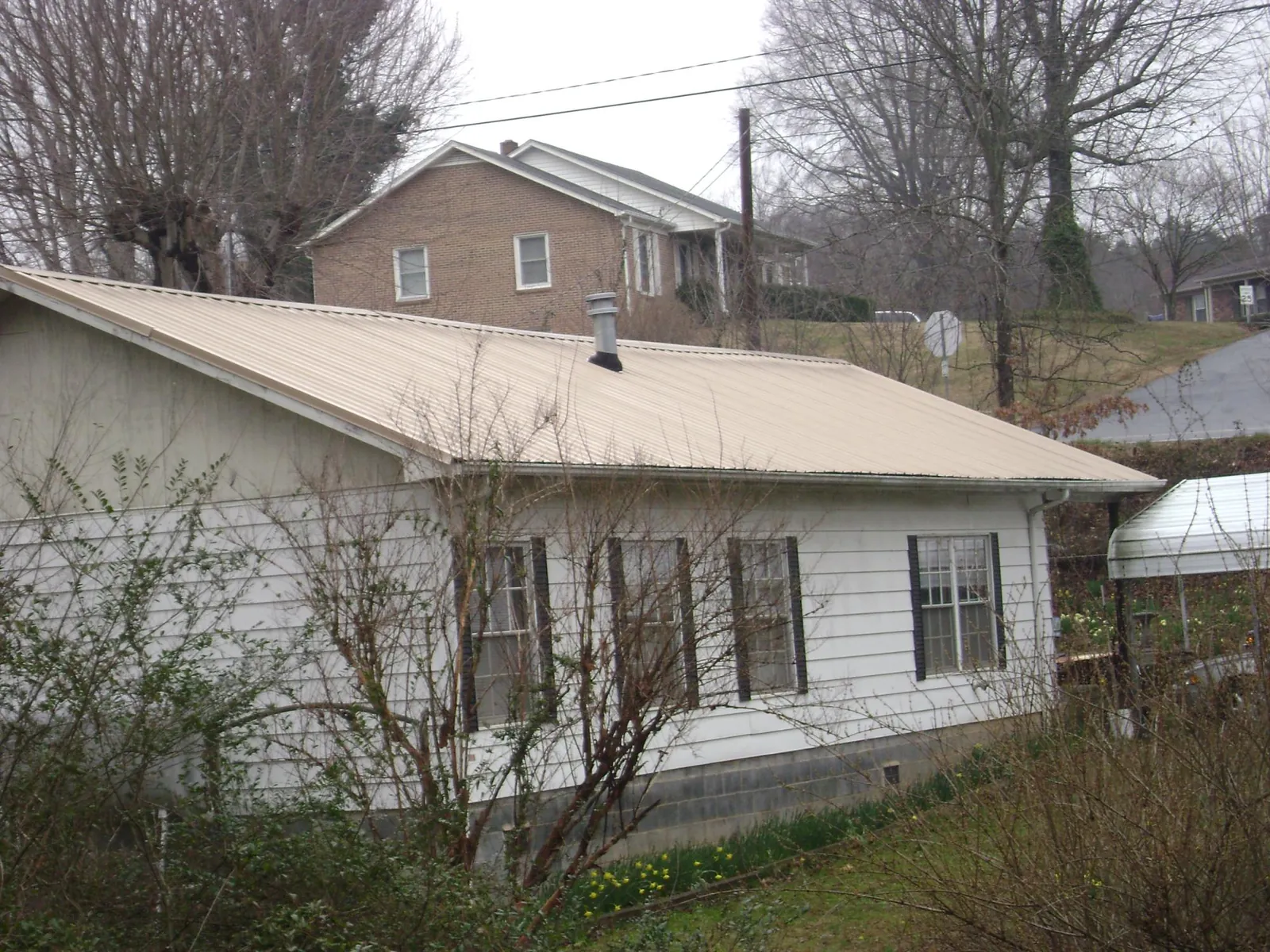 Tan metal roof on a white sided house set into a hillside — Commercial Roofing by Roofing Brothers in Bethany