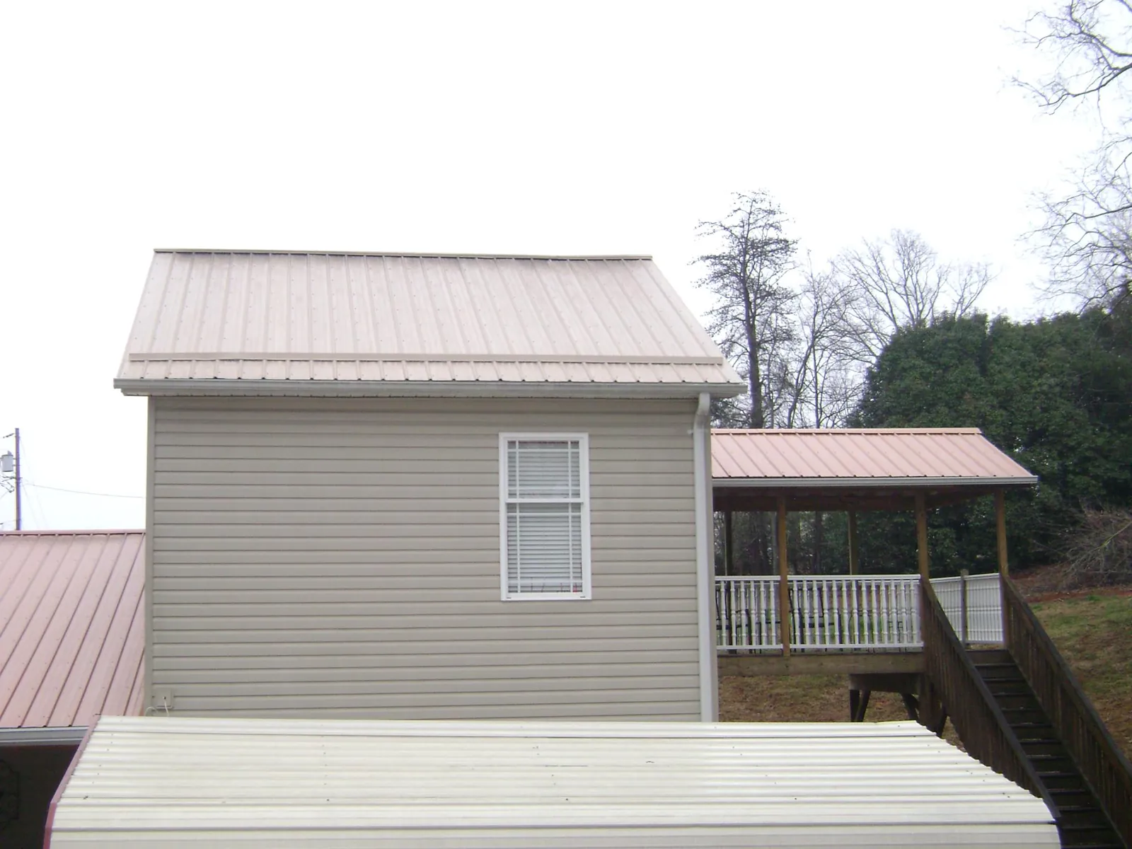 Tan metal roofs on a two story addition and attached porch, from a Roof Replacement job in Bethany